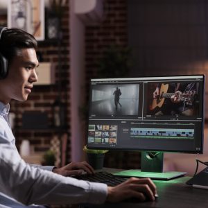 Male freelancer working on movie production with computer software, editing film montage with audio and visual effects. Creating multimedia content with footage, color grading creative app.